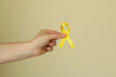 Female hand hold child cancer awareness ribbon on beige background