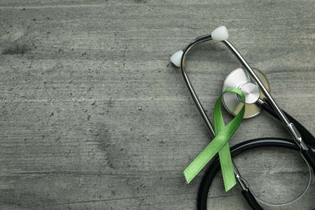 Green awareness ribbon and stethoscope on gray textured backgroundの写真素材