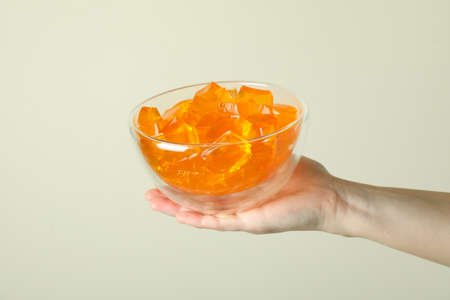Female hand hold bowl of orange jelly on beige backgroundの写真素材