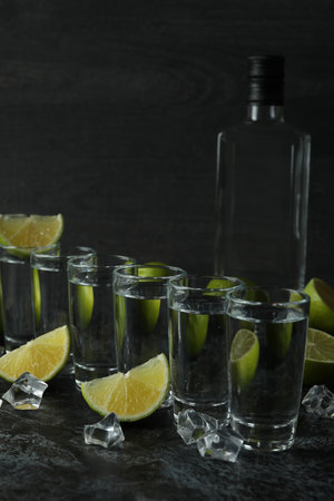 Bottle of vodka, shots, ice cubes and lime slices on black smokey tableの写真素材