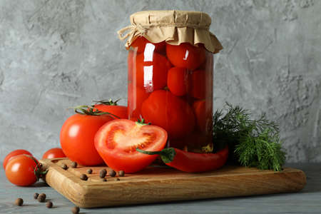 Board with jar of pickled tomatoes on wooden tableの写真素材