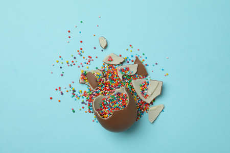 Broken easter chocolate egg with sprinkles on blue background