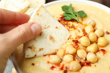 Female hand dips pita in tasty hummus, close up