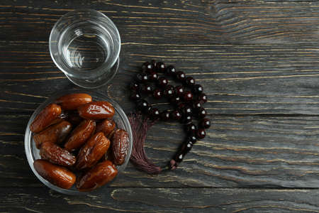 Glass of water, bowl of dates and rosary on wooden backgroundの写真素材