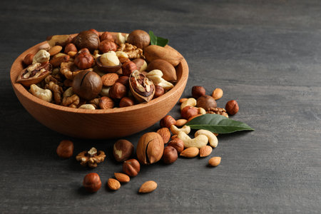 Wood bowl with different tasty nuts on gray wooden background