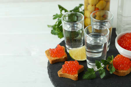 Shots of vodka and tasty snacks on white wooden background, space for textの写真素材
