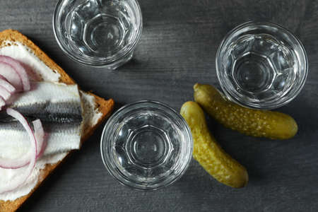 Shots of vodka and tasty snacks on dark wooden background