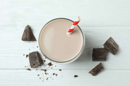 Glass of chocolate milkshake and chocolate pieces on white wooden tableの写真素材