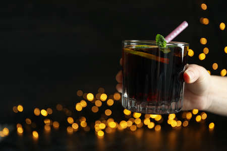 Female hand hold Cuba Libre against dark background with blurred lightsの写真素材