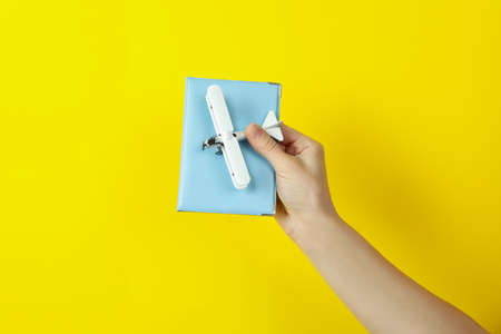 Female hand hold toy plane and passport on yellow background