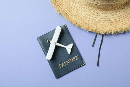 Passport, straw hat and toy plane on violet background