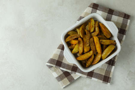 Bowl with fried potato on kitchen towel, on white textured background