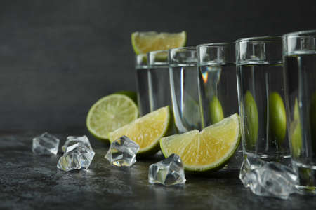Shots, ice cubes and lime slices on black smokey tableの写真素材