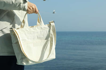 Woman in down jacket with stylish eco bag against seaの写真素材