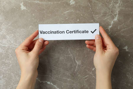 Female hands hold text Vaccination Certificate on gray textured backgroundの写真素材