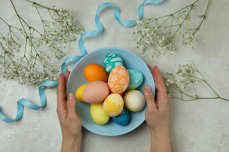 Female hands hold plate of colorful Easter eggs, top view