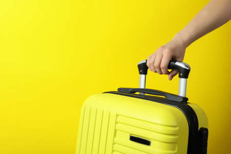 Female hand hold travel bag on yellow background