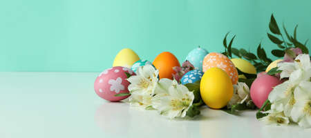 Color Easter eggs and alstroemeria flowers against mint background