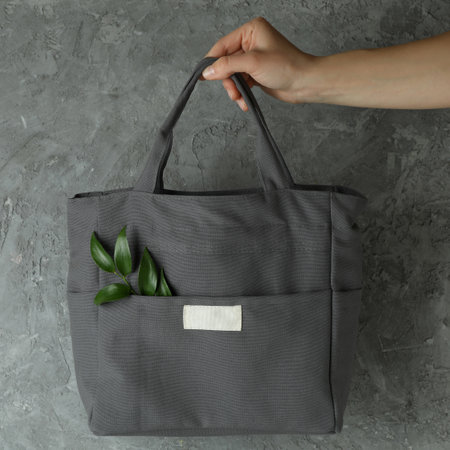Female hand hold stylish eco bag with twig against gray textured backgroundの写真素材