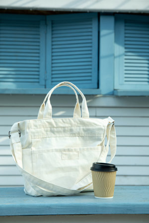 Stylish eco bag and paper cup outdoor on wooden counter
