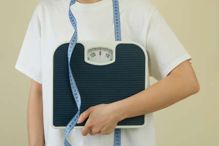 Woman with scales and measuring tape against beige backgroundの写真素材