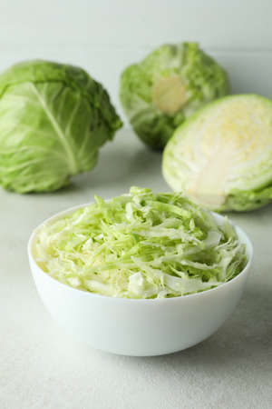 Bowl with sliced cabbage and fresh cabbage on white textured tableの写真素材