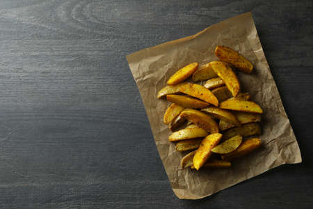 Baking paper with potato wedges on dark textured background