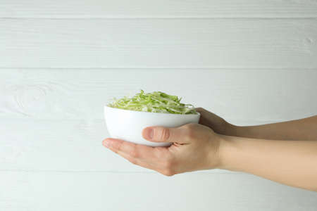 Female hands hold bowl with sliced cabbage on white wooden backgroundの写真素材