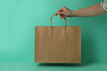 Female hand hold paper bag on mint backgroundの写真素材