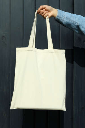 Female hand hold stylish eco bag on wooden background