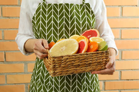 Woman hold basket of citrus against brick wall backgroundの写真素材