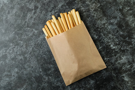 Paper bag with grissini breadsticks on black smoky background