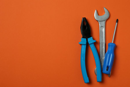 Screwdriver, wrench and pliers on orange background