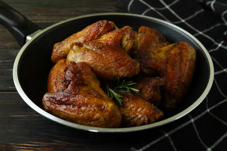 Pan with baked chicken wings and kitchen towel on wooden backgroundの写真素材