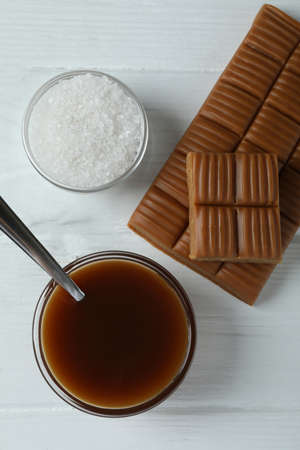 Caramel sauce, bar and salt on white wooden background