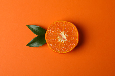 Half of mandarin with leaves on orange backgroundの写真素材