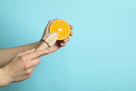 Female hands hold orange and juicer on blue background