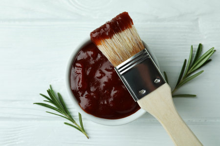 Bowl of barbecue sauce with brush and rosemary on white wooden tableの写真素材