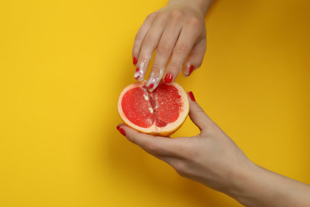 Female hands hold grapefruit with condensed milk on yellow backgroundの写真素材