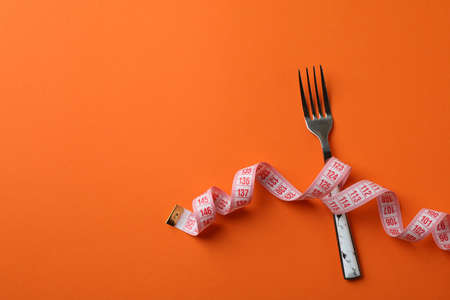 Fork with measuring tape on orange backgroundの写真素材