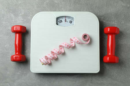 Scales, dumbbells and measuring tape on gray background