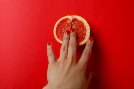 Female hand and grapefruit on red backgroundの写真素材