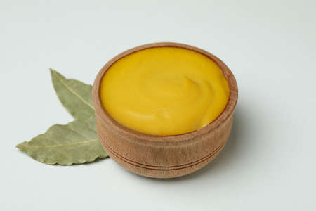 Wooden bowl with mustard and leaves on white backgroundの写真素材
