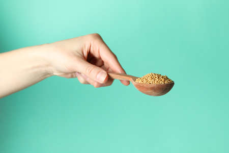 Female hand hold spoon with mustard seeds on mint backgroundの写真素材