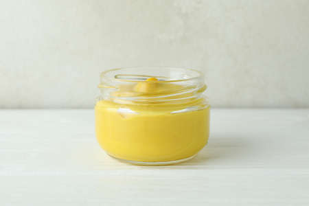 Glass jar with mustard on white wooden table