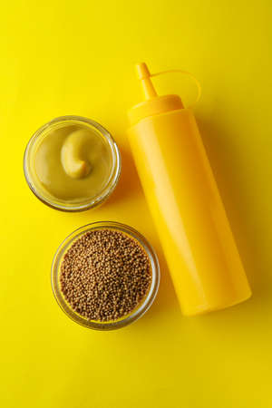 Bowls with mustard and sauce bottle on yellow background