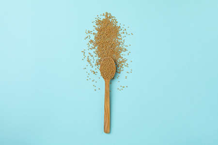 Wooden spoon with mustard seeds on blue background