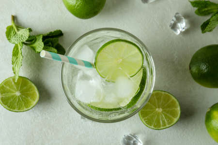 Glass of mojito cocktail and ingredients on white textured background