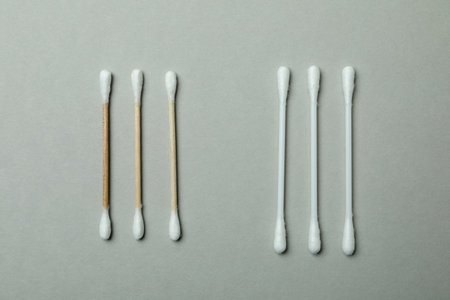 Wooden and plastic cotton swabs on light gray background