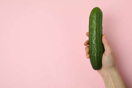 Female hand hold ripe cucumber on pink backgroundの写真素材